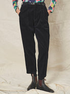 Person wearing black corduroy pants and colourful shirt on a neutral background