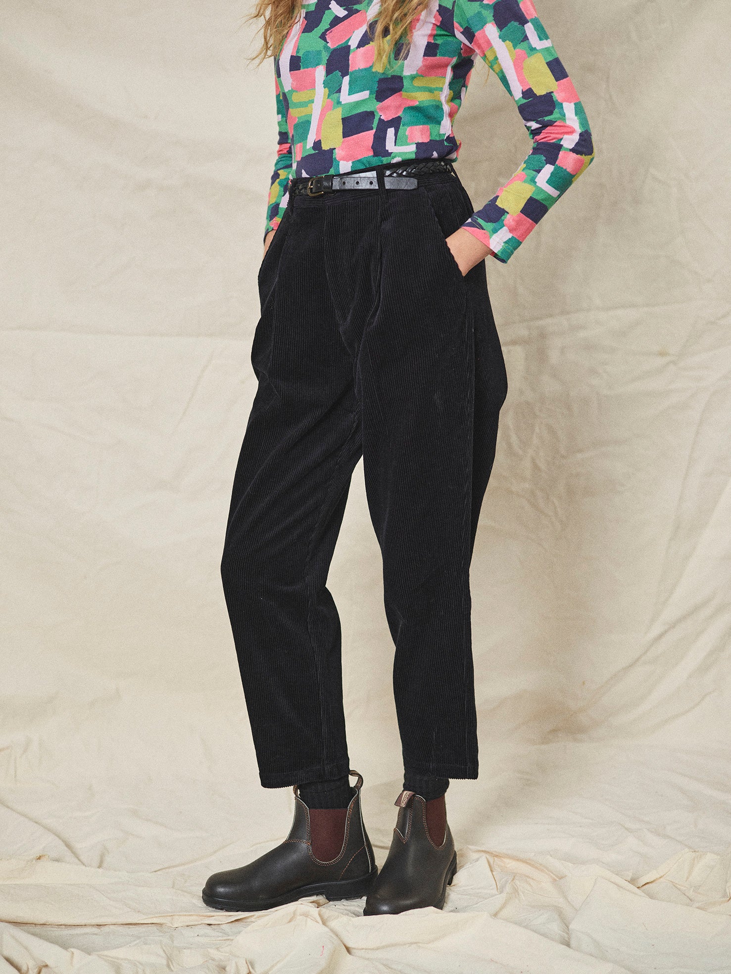 Person wearing black corduroy pants and colourful shirt on a neutral background