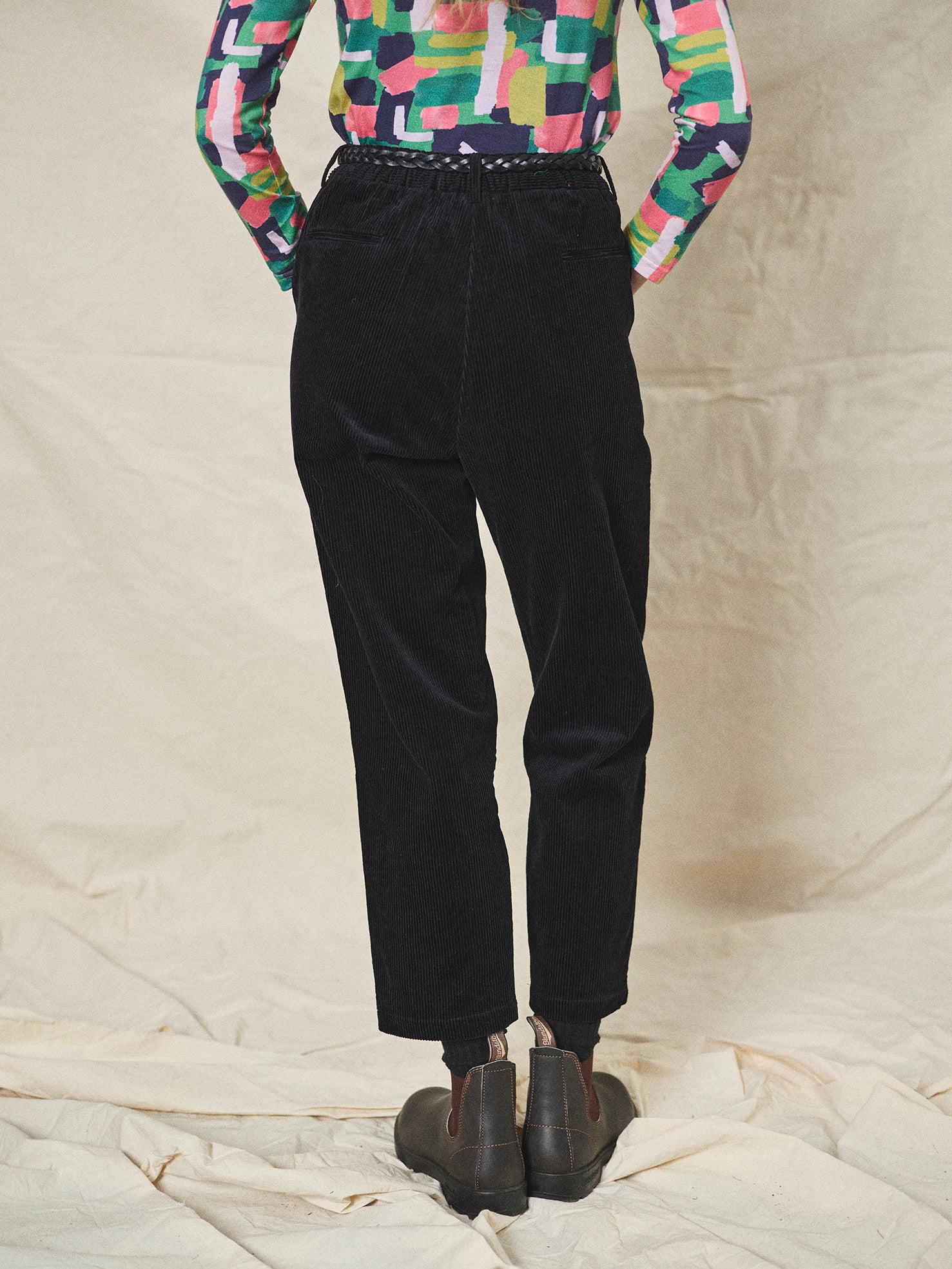 Person wearing black corduroy pants and colourful shirt on a neutral background