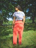 A pair of red cotton linen trousers with side welt pockets and a row of buttons down the front.