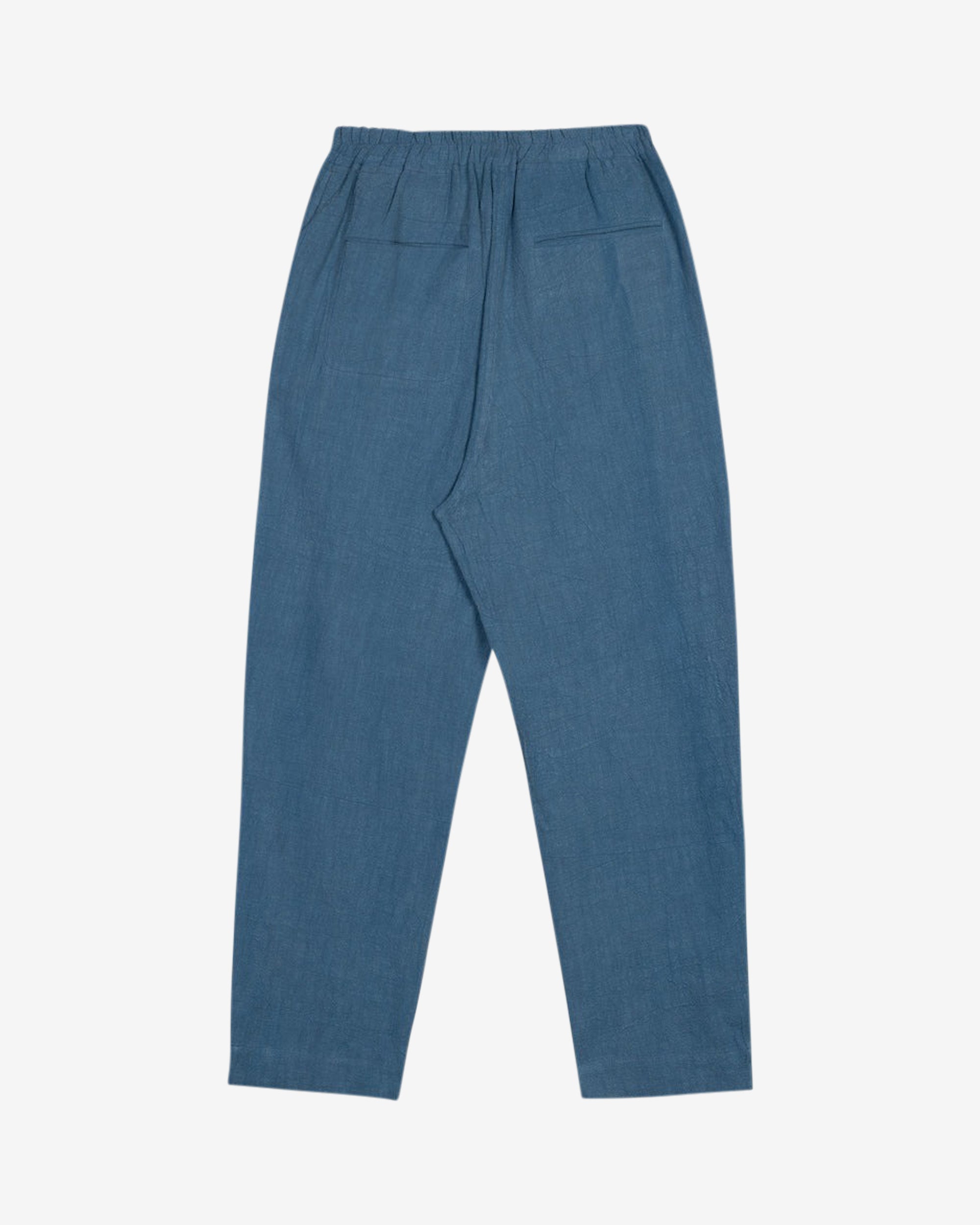 Washed blue cotton linen trousers with side welt pockets and elasticated waist at the back, featuring five corozo buttons down the front.