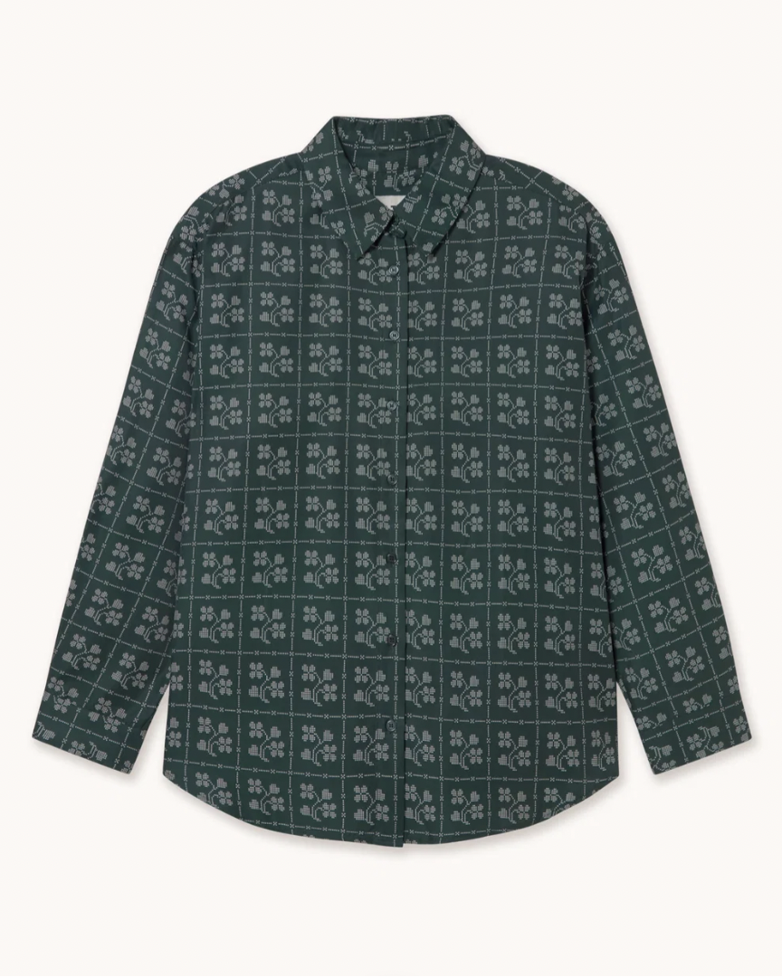 A long-sleeve button-up shirt with a dark green base and a repeating white floral block print, laid flat against a light off-white background.