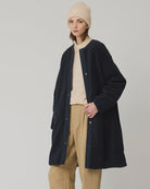A model stands against a light gray studio background wearing a long navy cardigan over a cream turtleneck, beige wide-leg trousers, a beige beanie, and dark brown loafers.