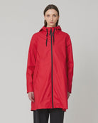 A model stands against a light gray studio background wearing a bright red hooded raincoat with a black front zipper and black drawstrings, paired with black pants and blue sneakers.