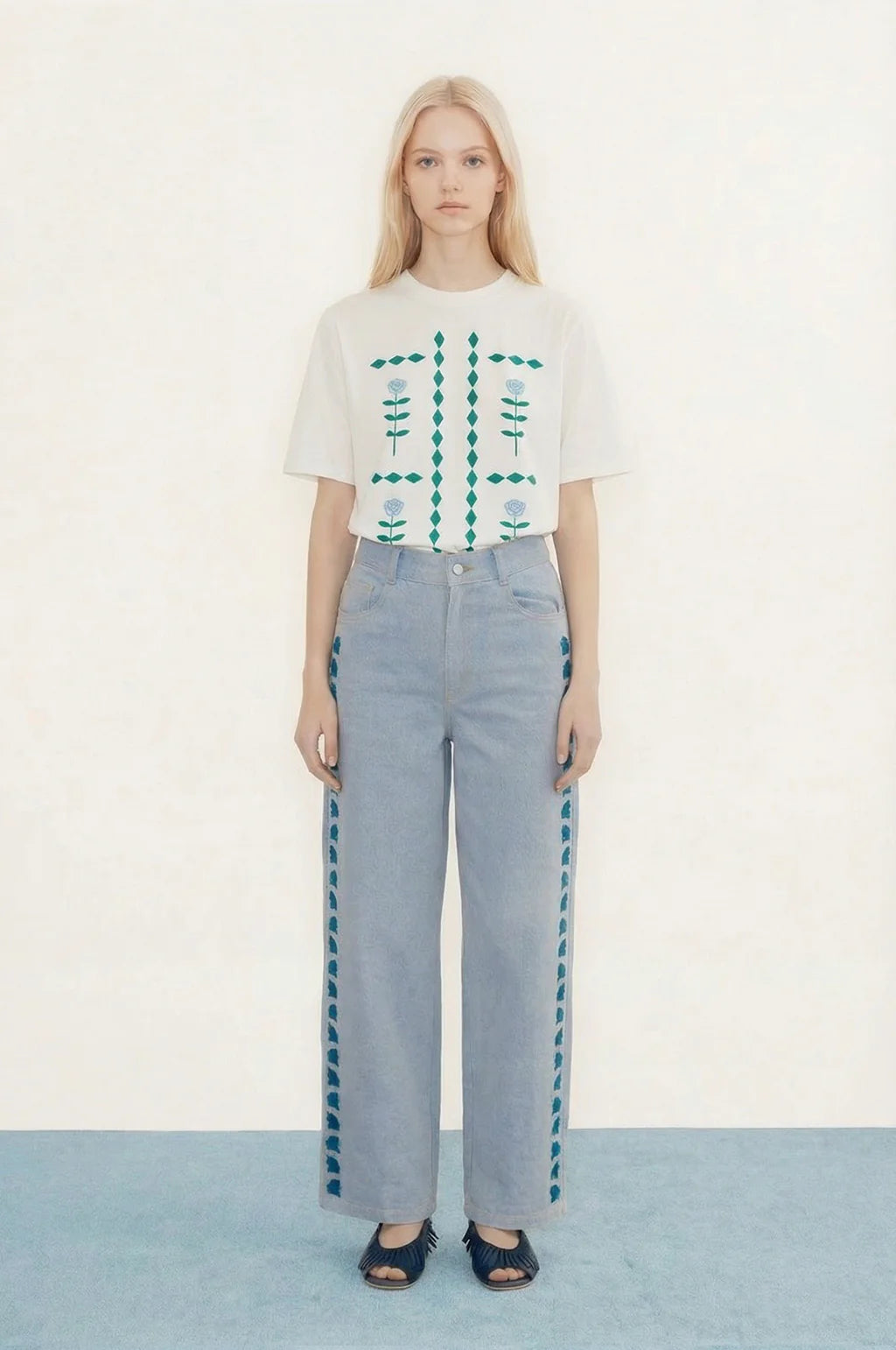 Woman wearing a white floral top and light blue pants on a plain background