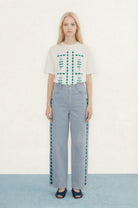 Woman wearing a white floral top and light blue pants on a plain background