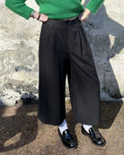A person wearing black lyocell wide-leg trousers and a green top, standing against a textured background.