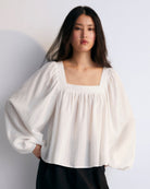 A white Tencel blouse with a square neckline, long sleeves, and elastic cuffs on a plain background.