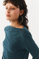 Woman wearing a teal long-sleeve top against a white background