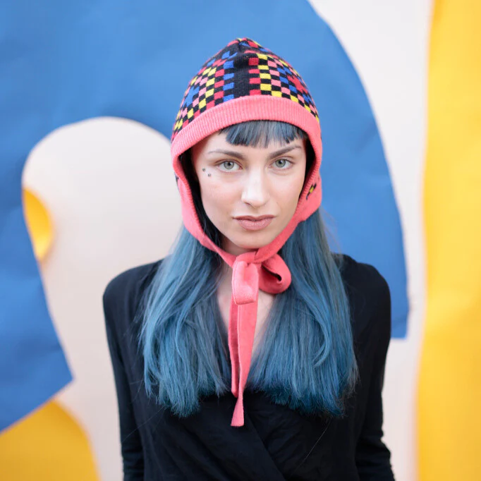 Person wearing a colorful helmet with a pink chin strap against a multicolored background