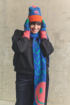 Person wearing a colorful knitted hat and scarf against a concrete wall.