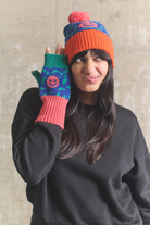 Person wearing colorful knit hat and gloves against a textured wall.