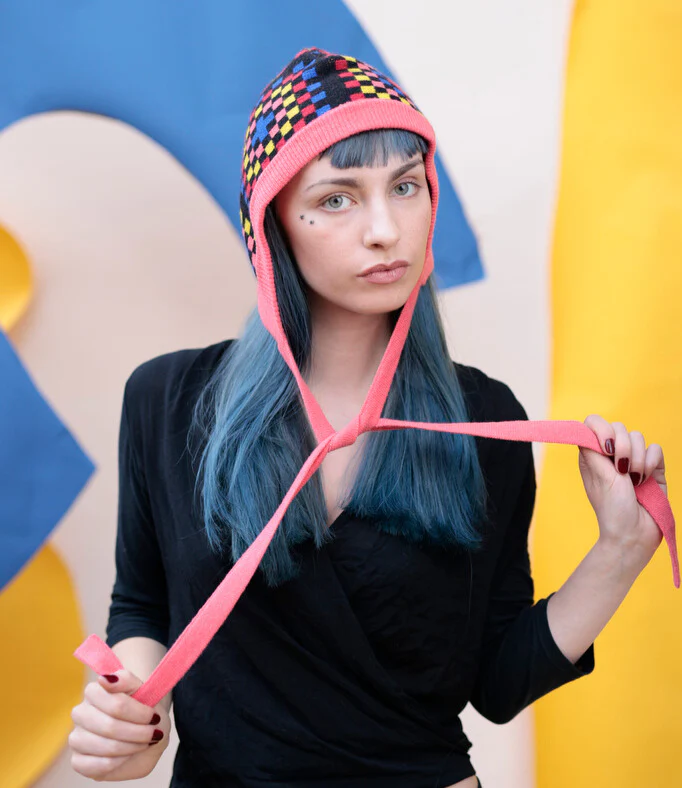 Person wearing a colorful knit hat with a pink strap against a multicolored background