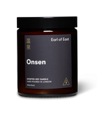A hand-poured soy wax candle in an amber glass jar with a black label reading 'EARL OF EAST ONSEN'