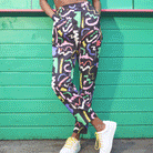A pair of black holiday trousers with a multicolored scribble print, featuring a high waist, tapered leg, and side pockets.
