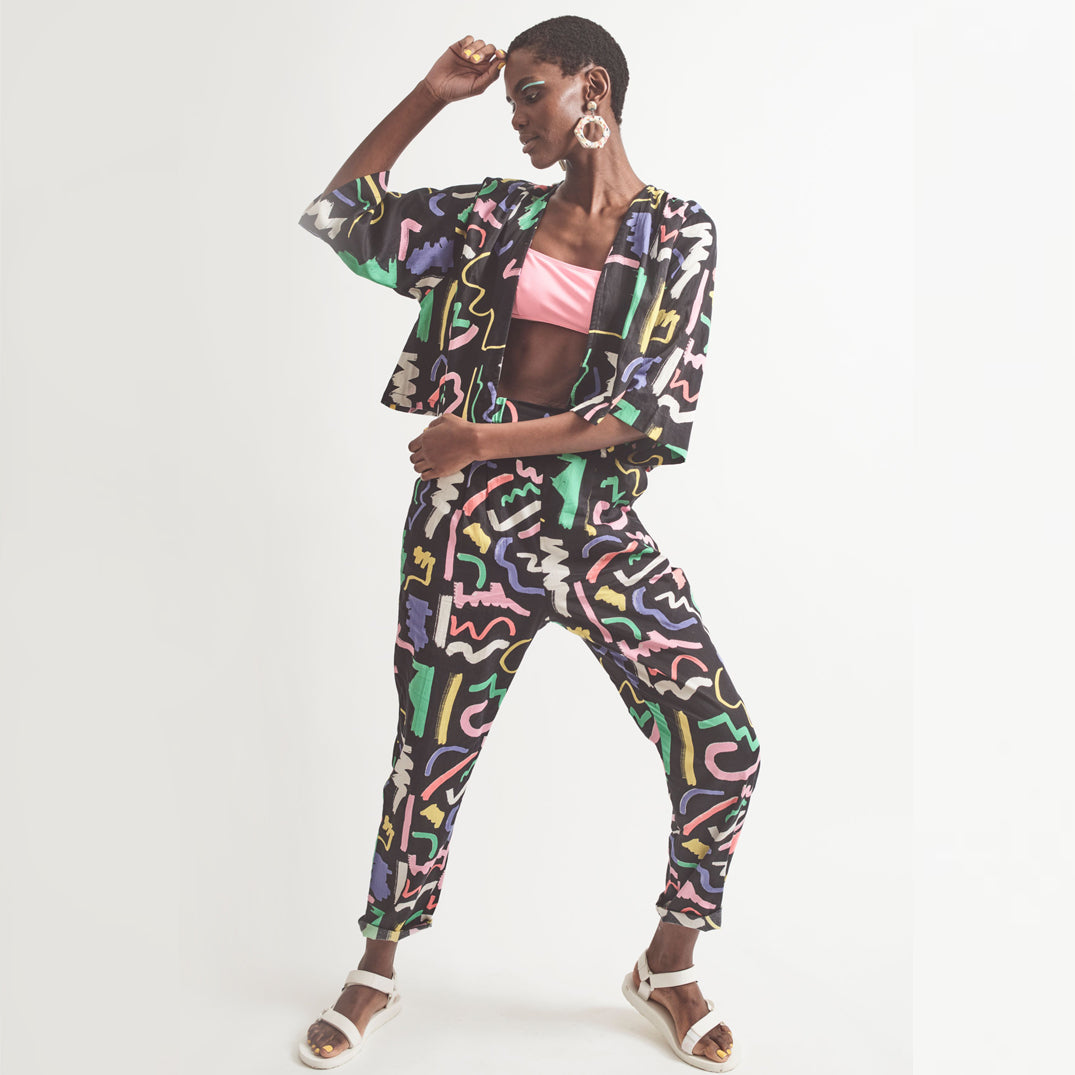 A pair of black holiday trousers with a multicolored scribble print, featuring a high waist, tapered leg, and side pockets.
